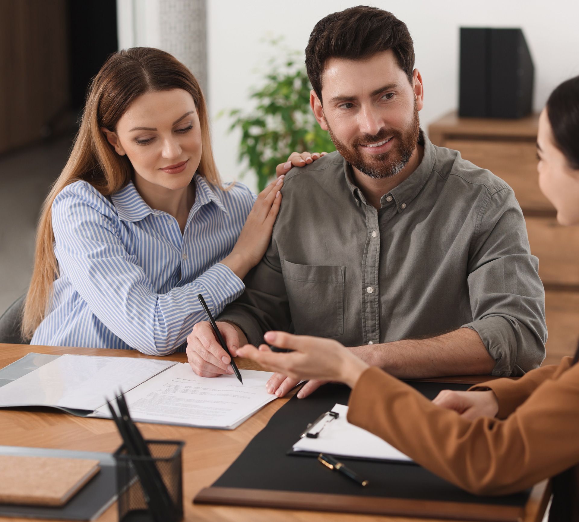 Couple signing documents with a professional, smiling, indoors.