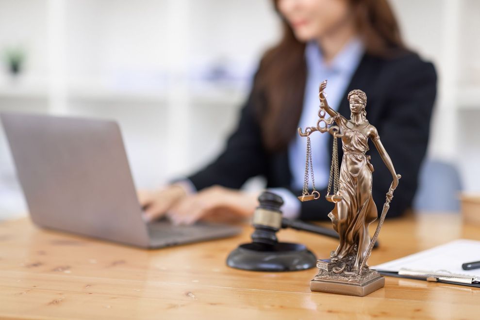 Statue of Lady Justice on desk with laptop and lawyer in background.