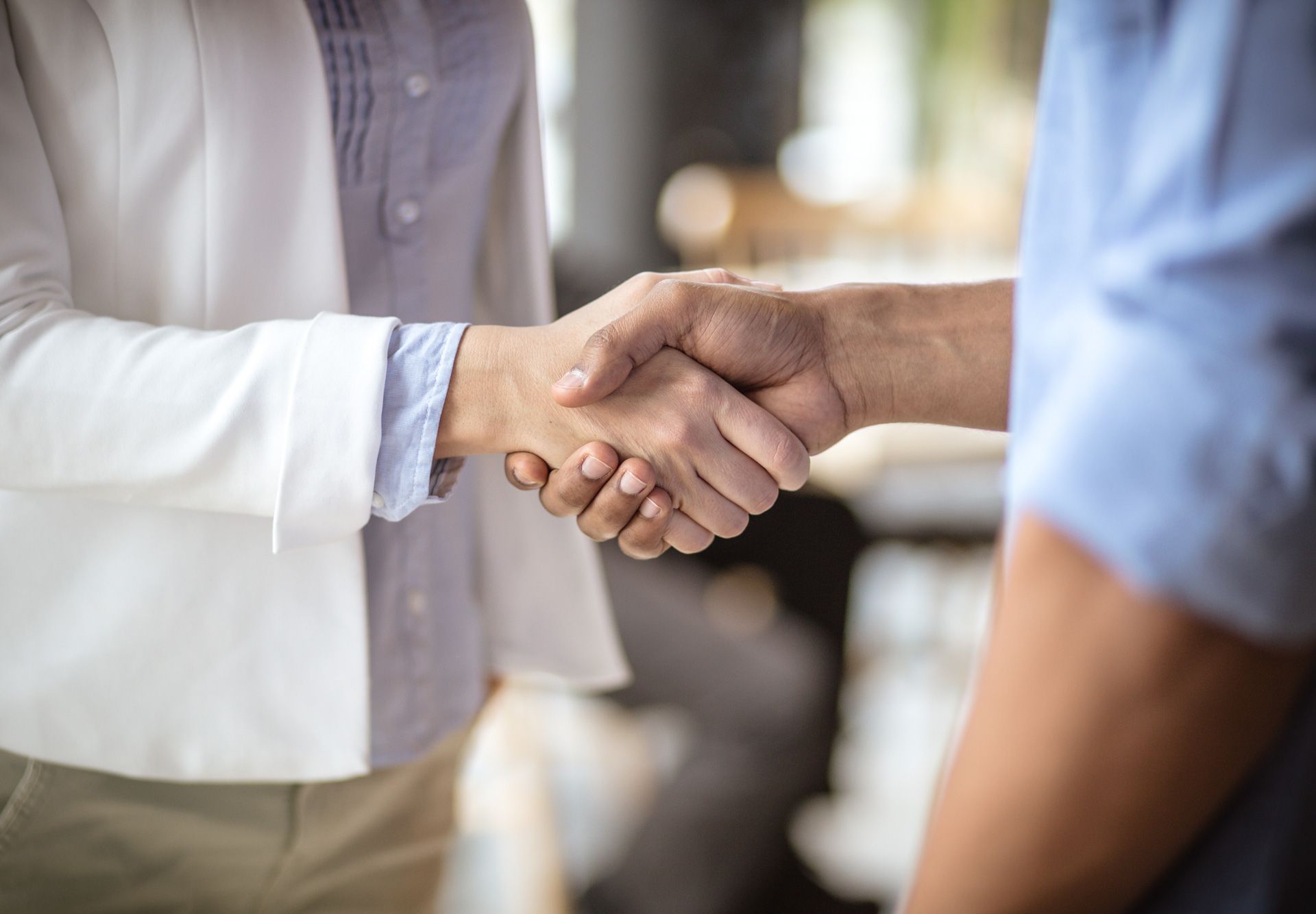 Two people shaking hands, indoors. Woman in white blazer, man in blue shirt.