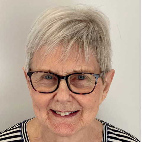Woman with short gray hair and glasses smiles at the camera. She wears a striped shirt.