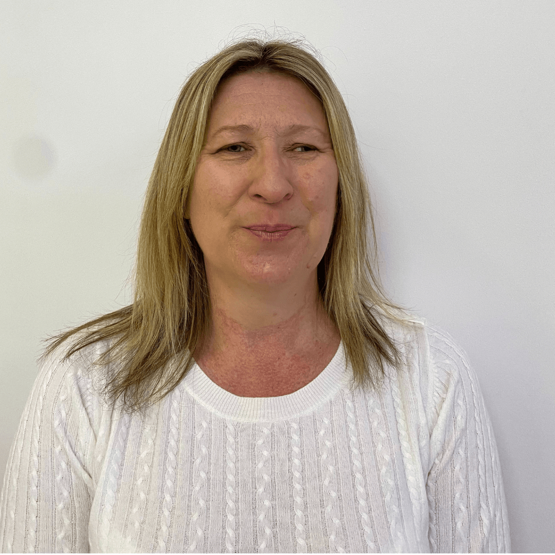 Woman with blonde hair wearing a white sweater, smiling in front of a white wall.