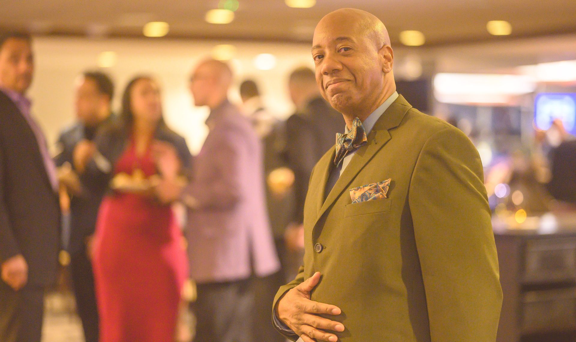 A man in a green suit and tie is standing in front of a crowd of people.