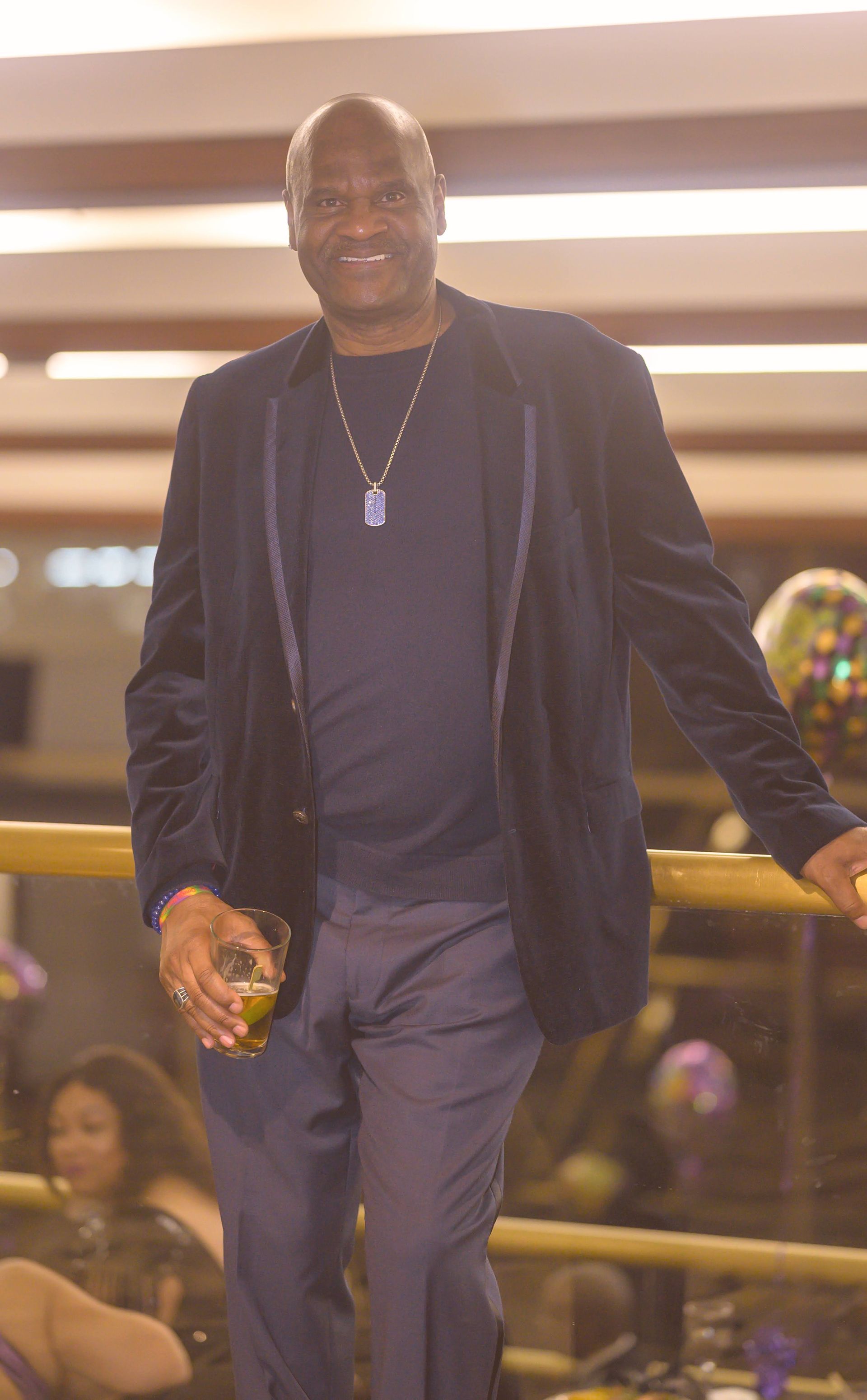 A man in a suit is standing next to a railing holding a glass of beer.