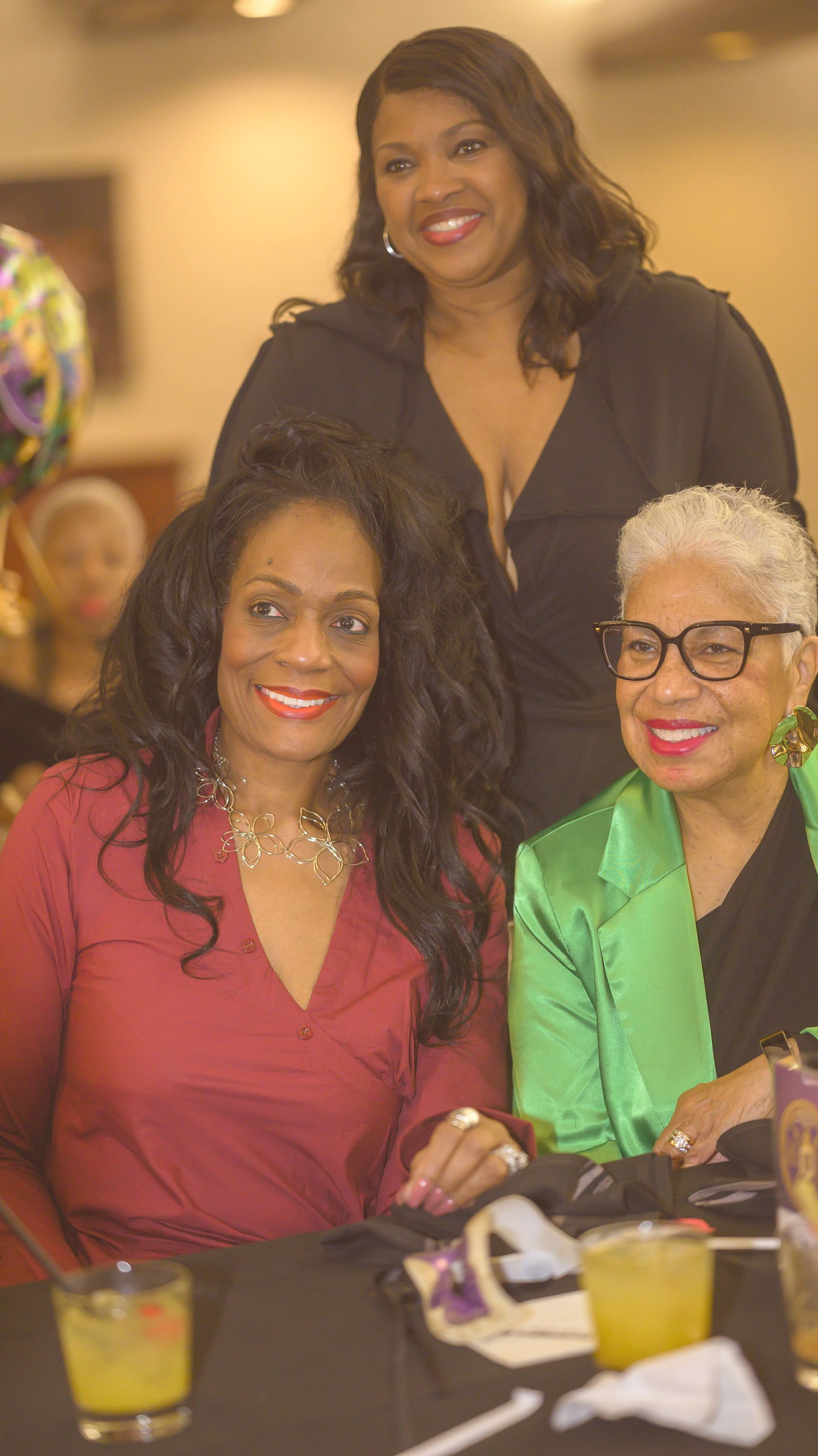 Three women are posing for a picture while sitting at a table.
