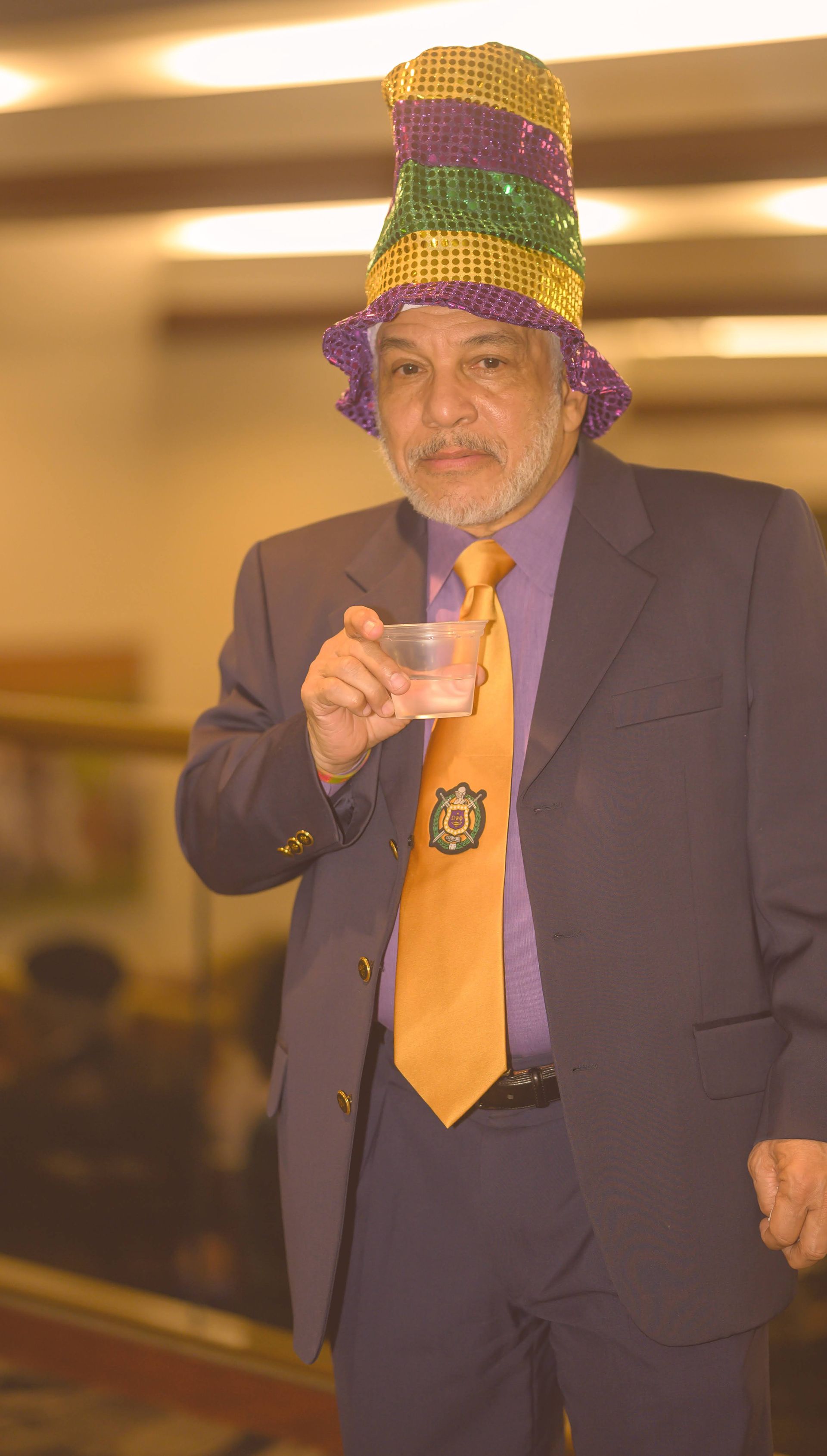 A man in a suit and tie is wearing a mardi gras hat.