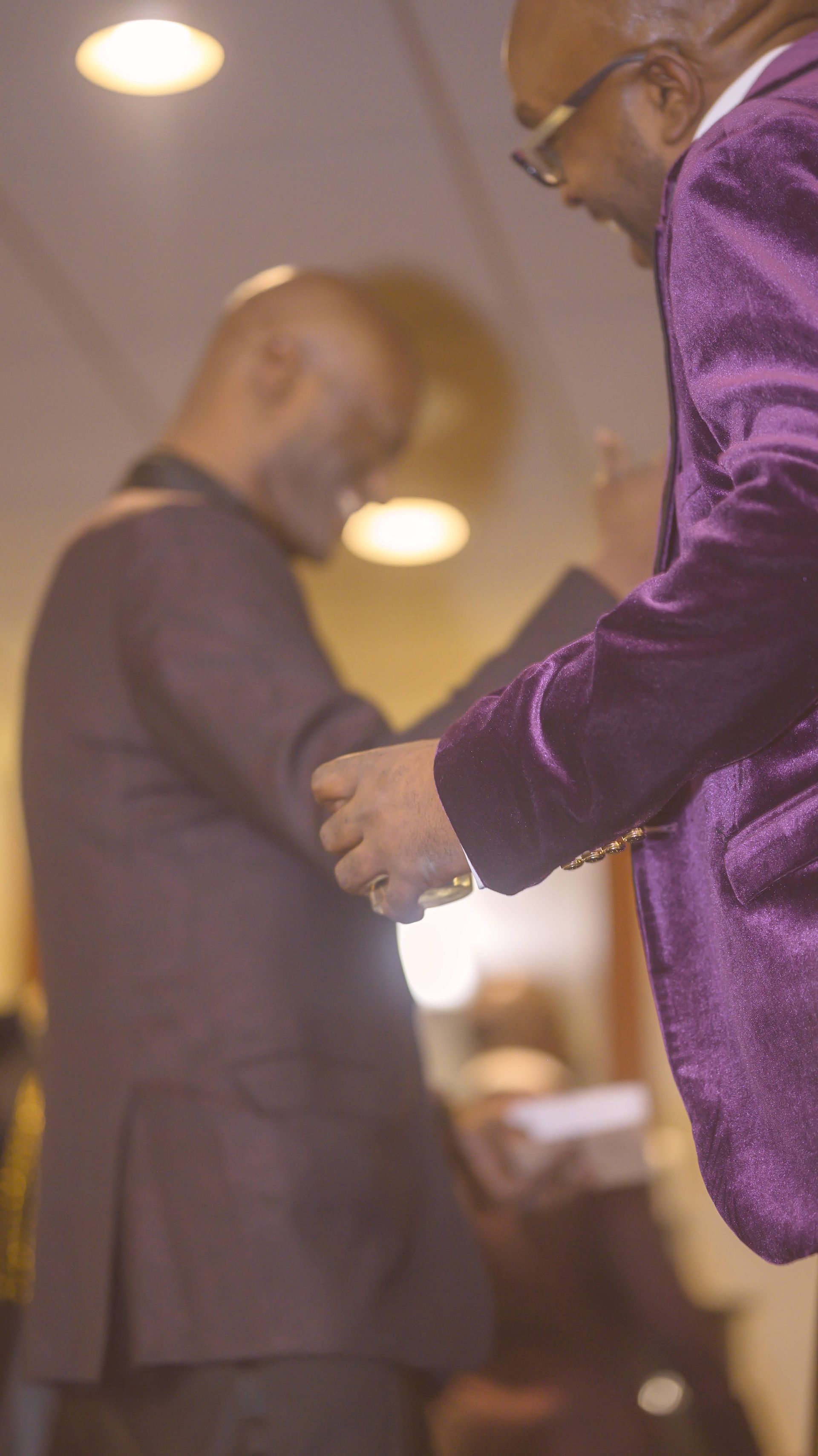 A man in a purple suit is shaking hands with another man in a black suit.