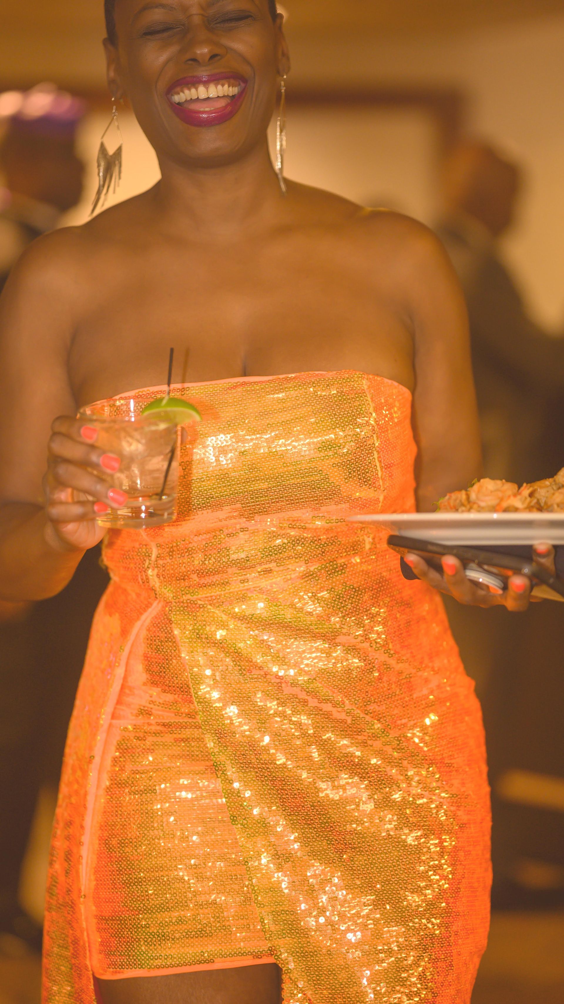 A woman in an orange dress is holding a tray of food and a drink.