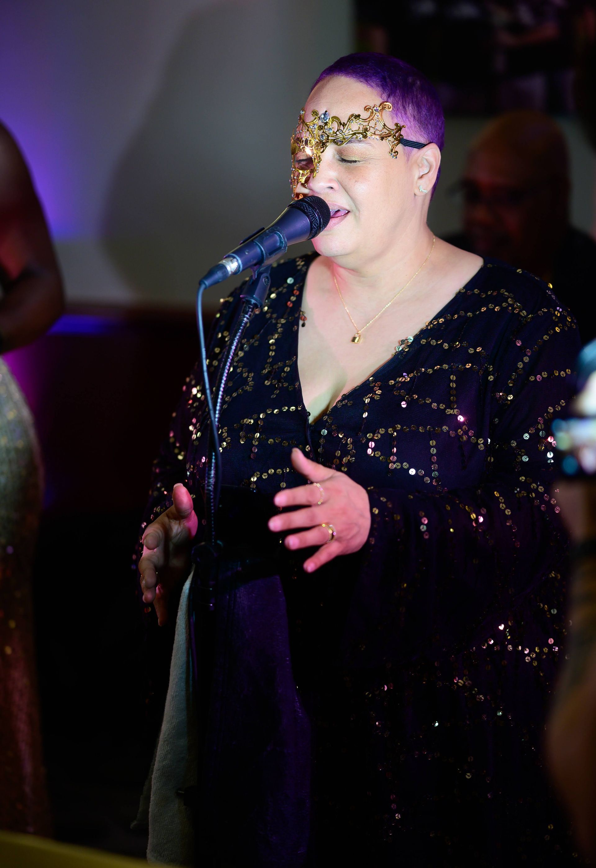 A woman wearing a mask is singing into a microphone.