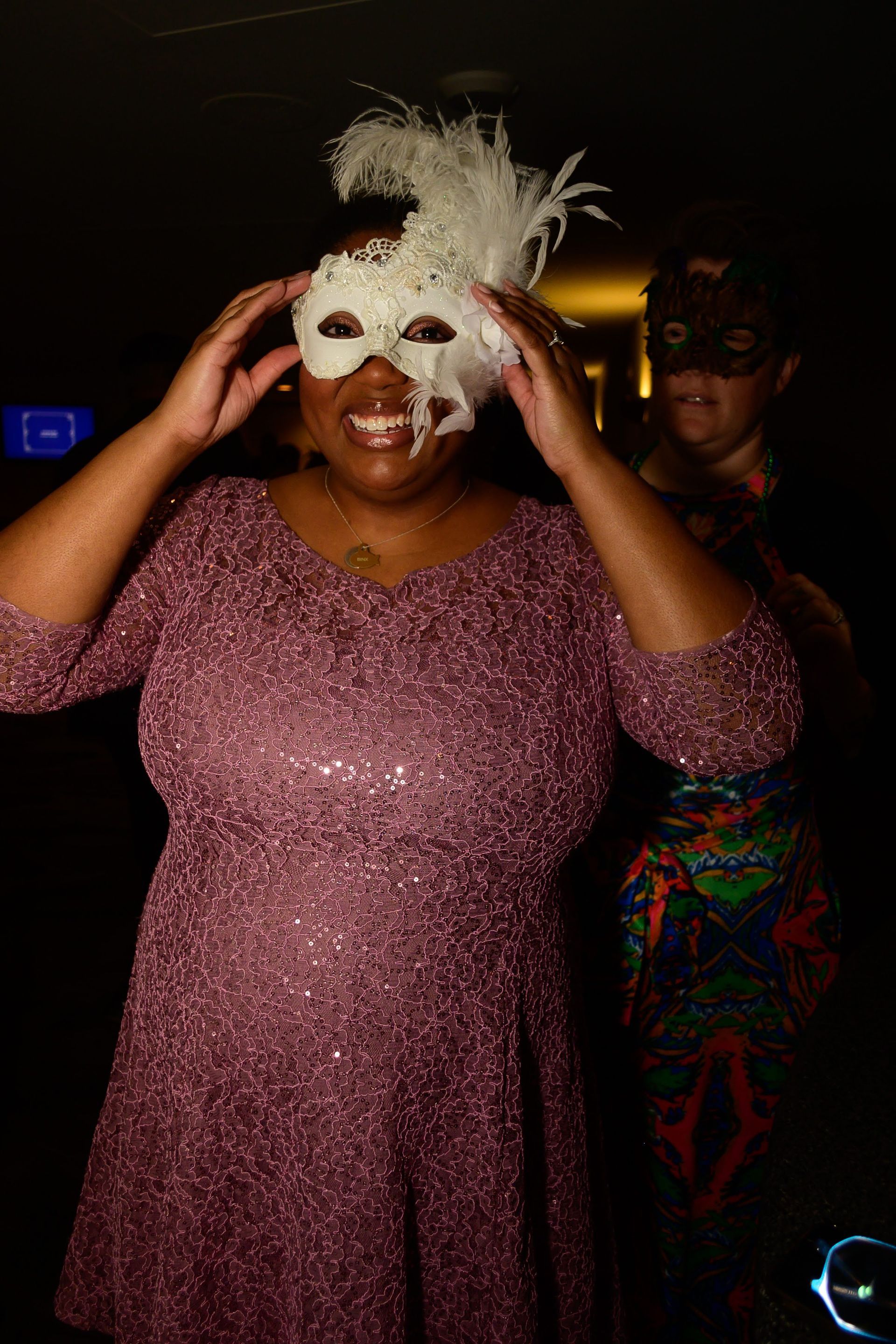 A woman in a purple dress is wearing a white mask.