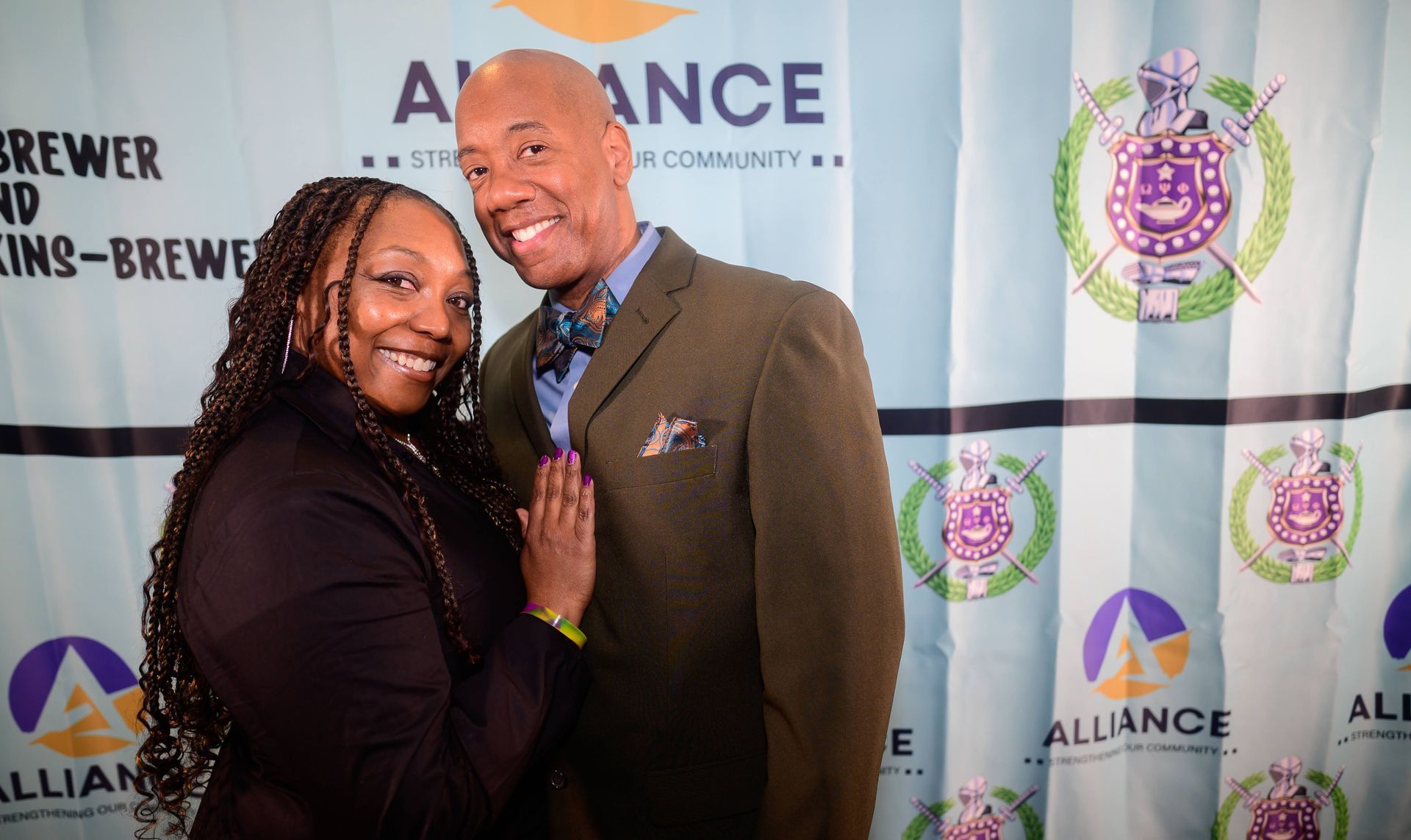 A man and a woman are posing for a picture in front of a banner that says alliance.