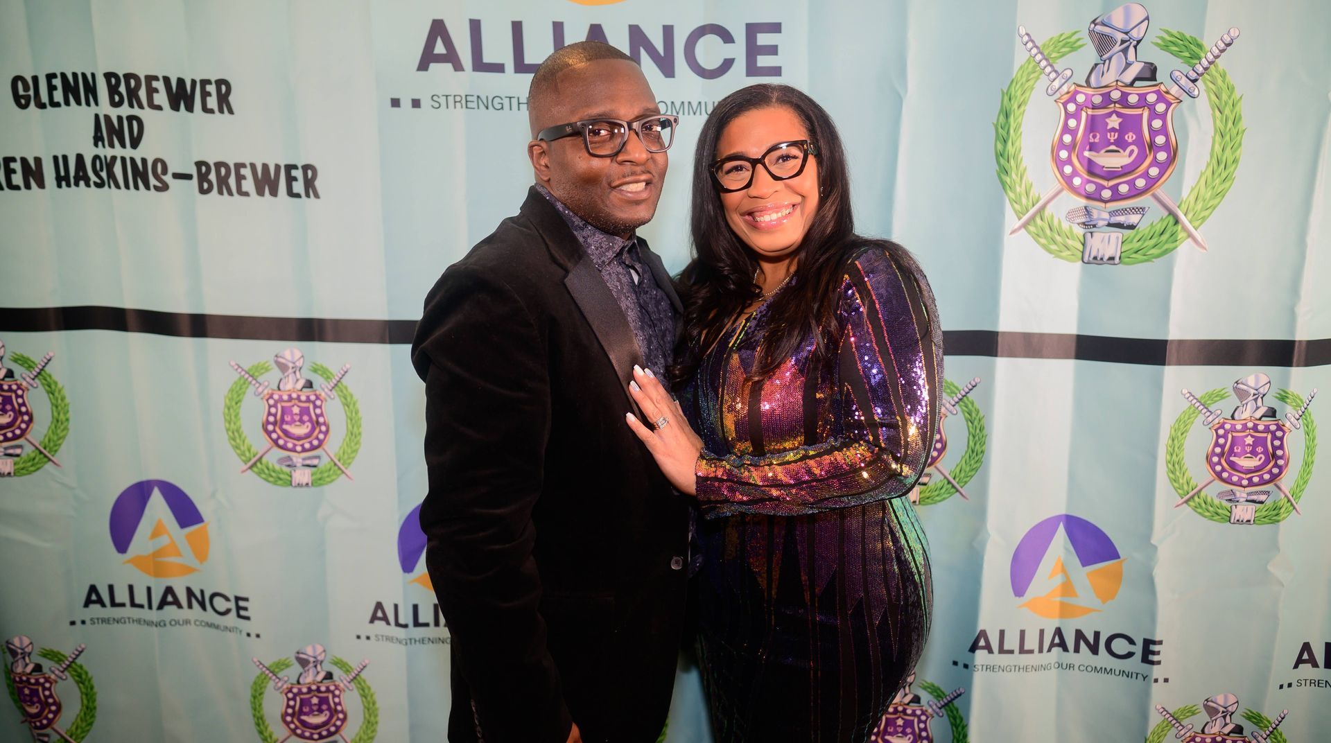 A man and a woman are posing for a picture in front of a alliance banner.