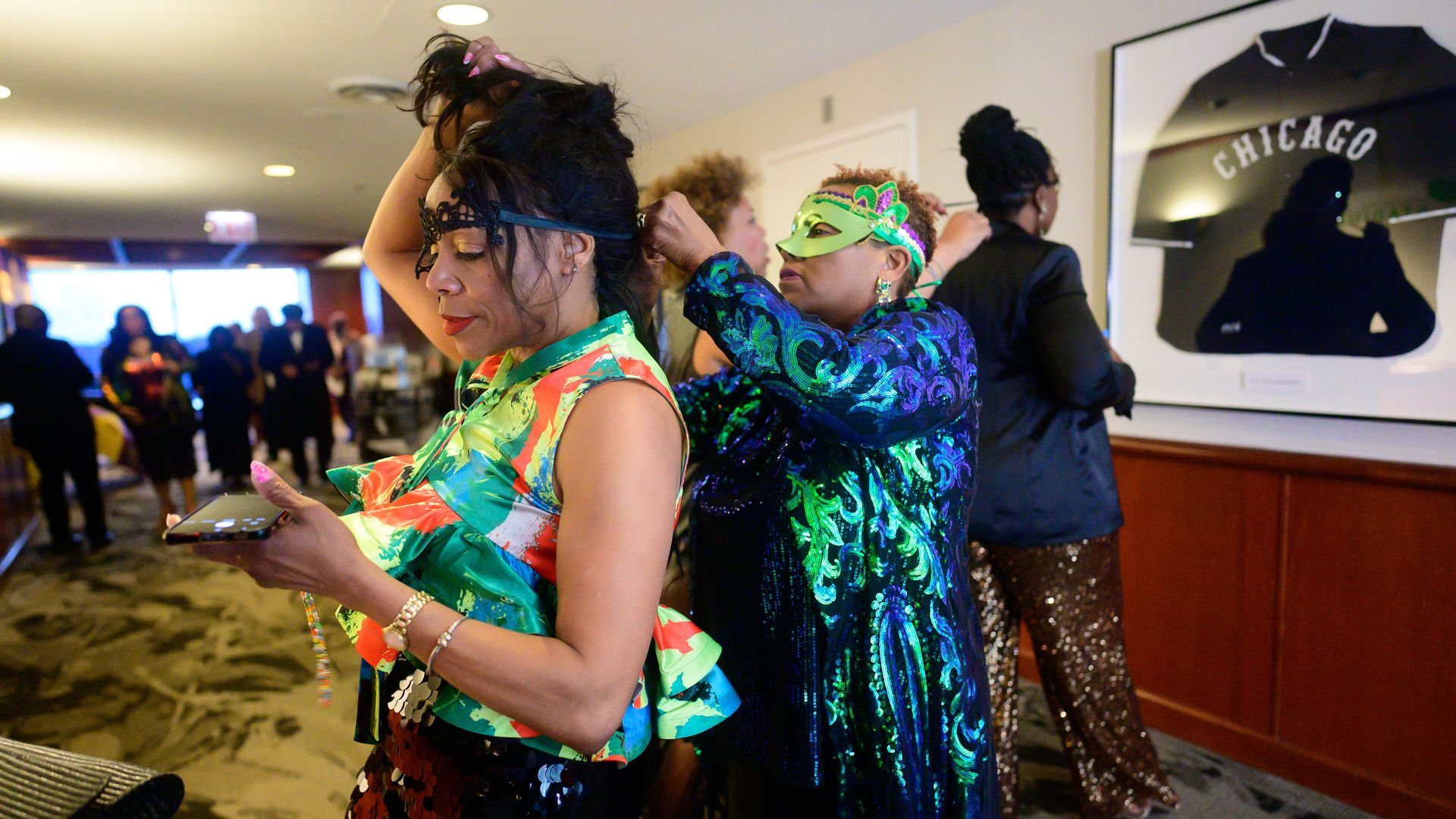 A group of women are standing in a room and one of them is looking at her phone.