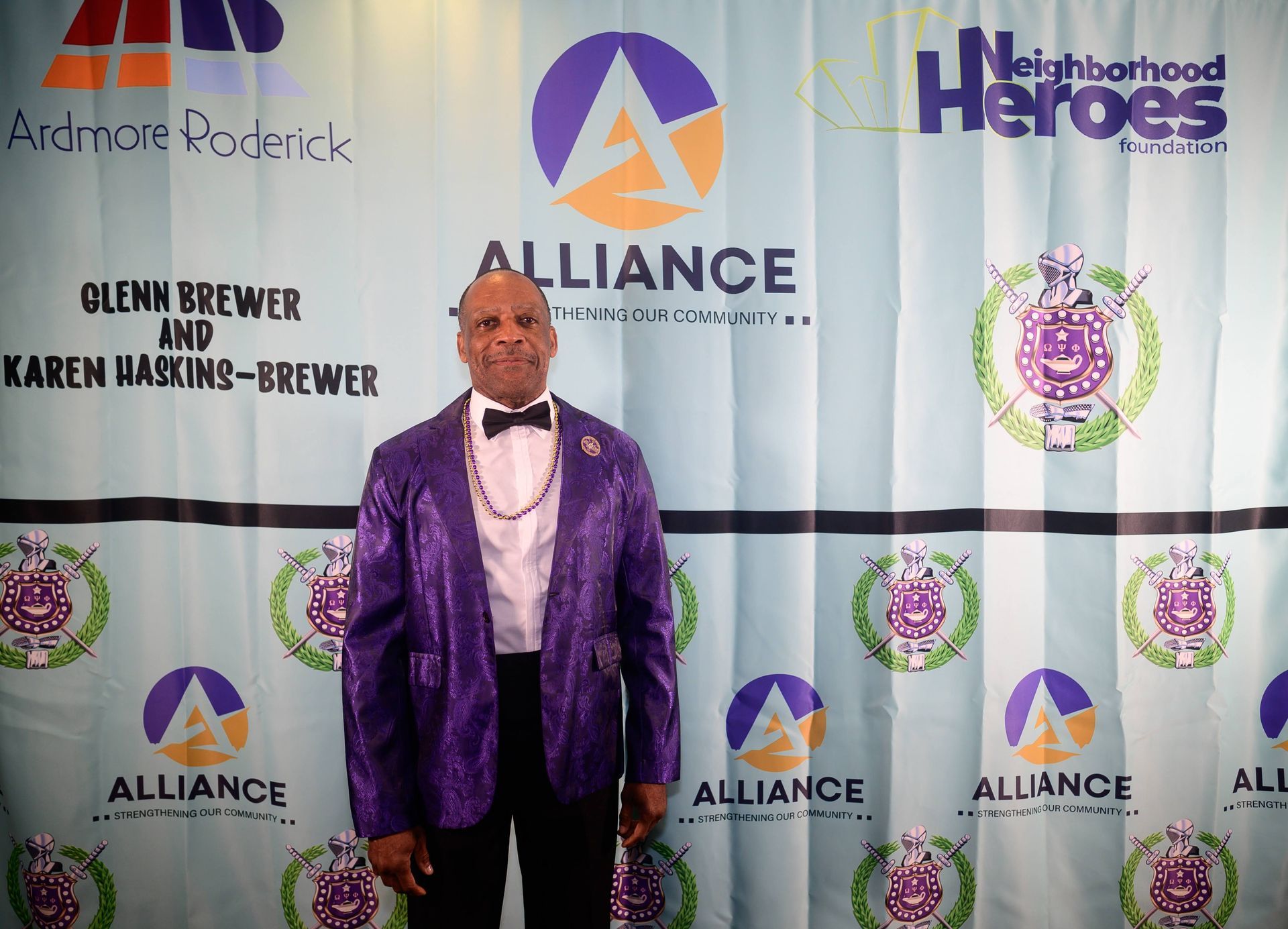 A man in a purple suit is standing in front of a wall that says neighborhood heroes