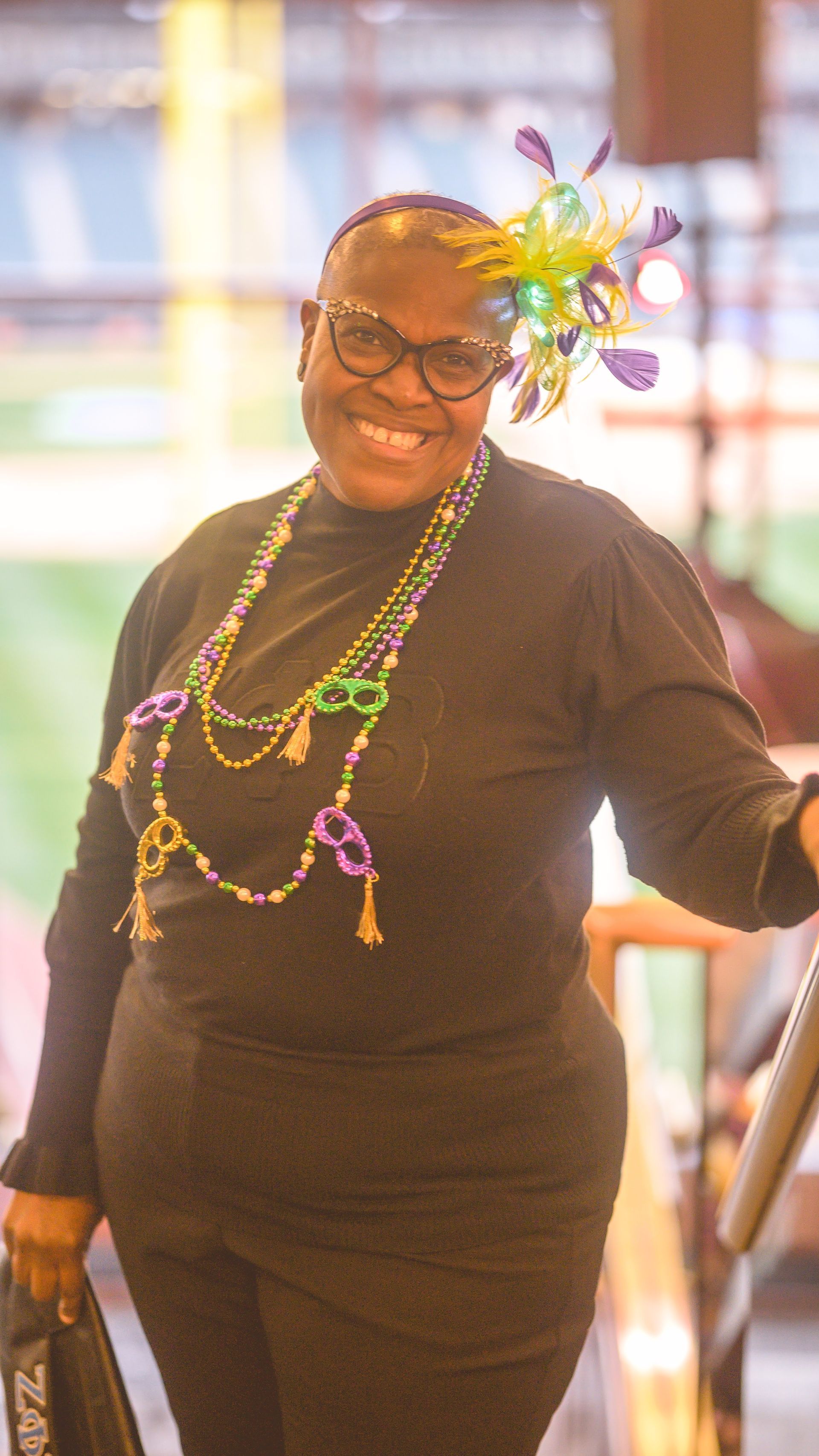 A woman wearing a mardi gras hat and necklace is standing on a set of stairs.