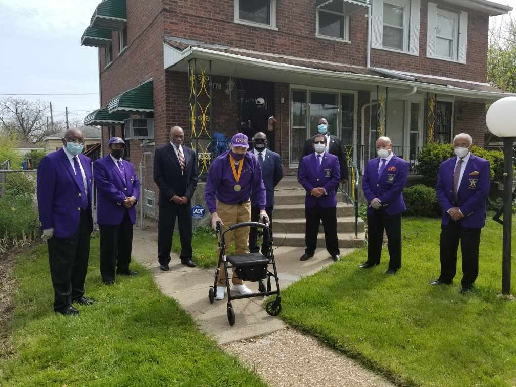 A group of men in purple suits are standing in front of a house.