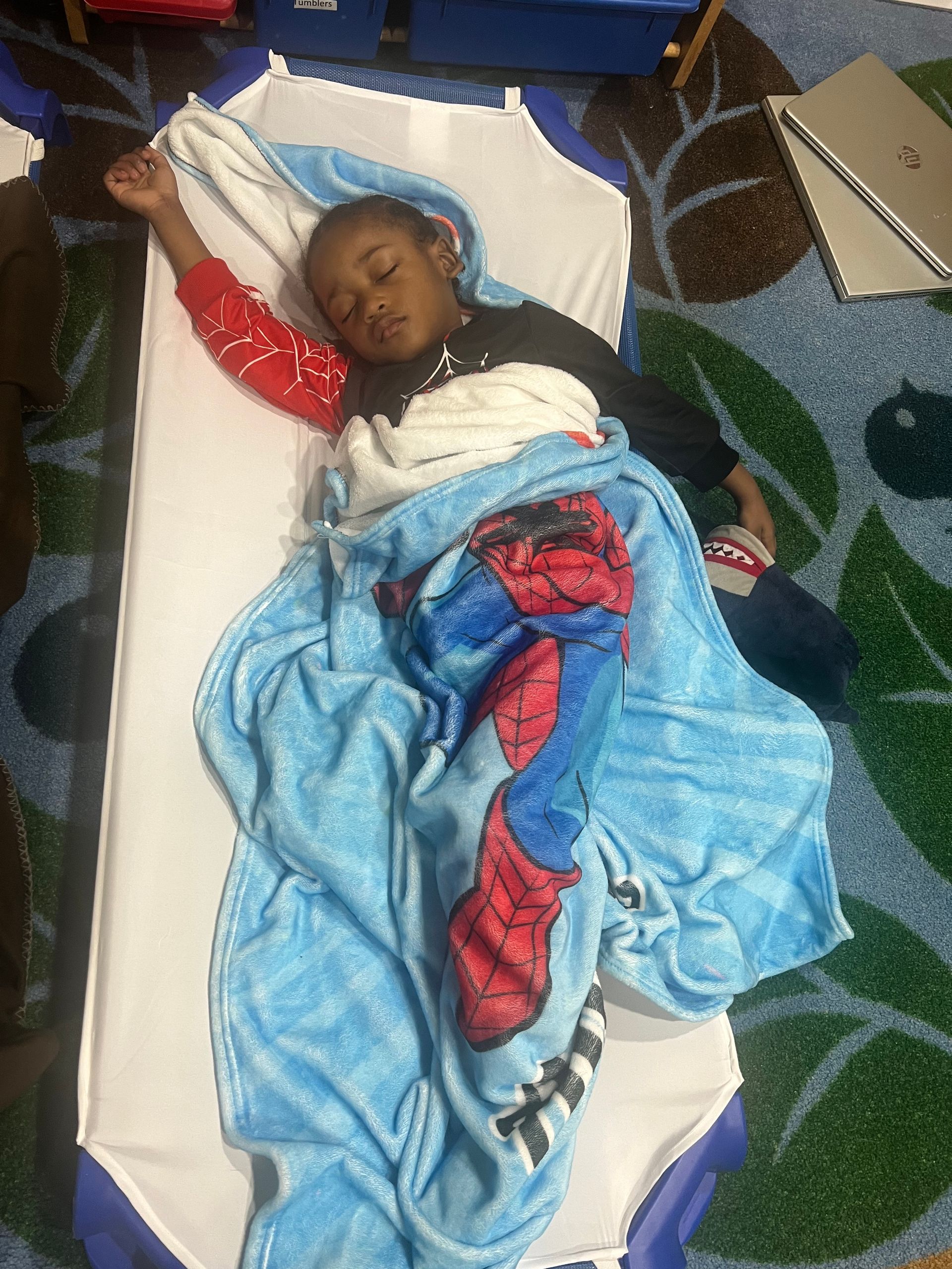 A young boy is sleeping on a bed with a spiderman blanket.