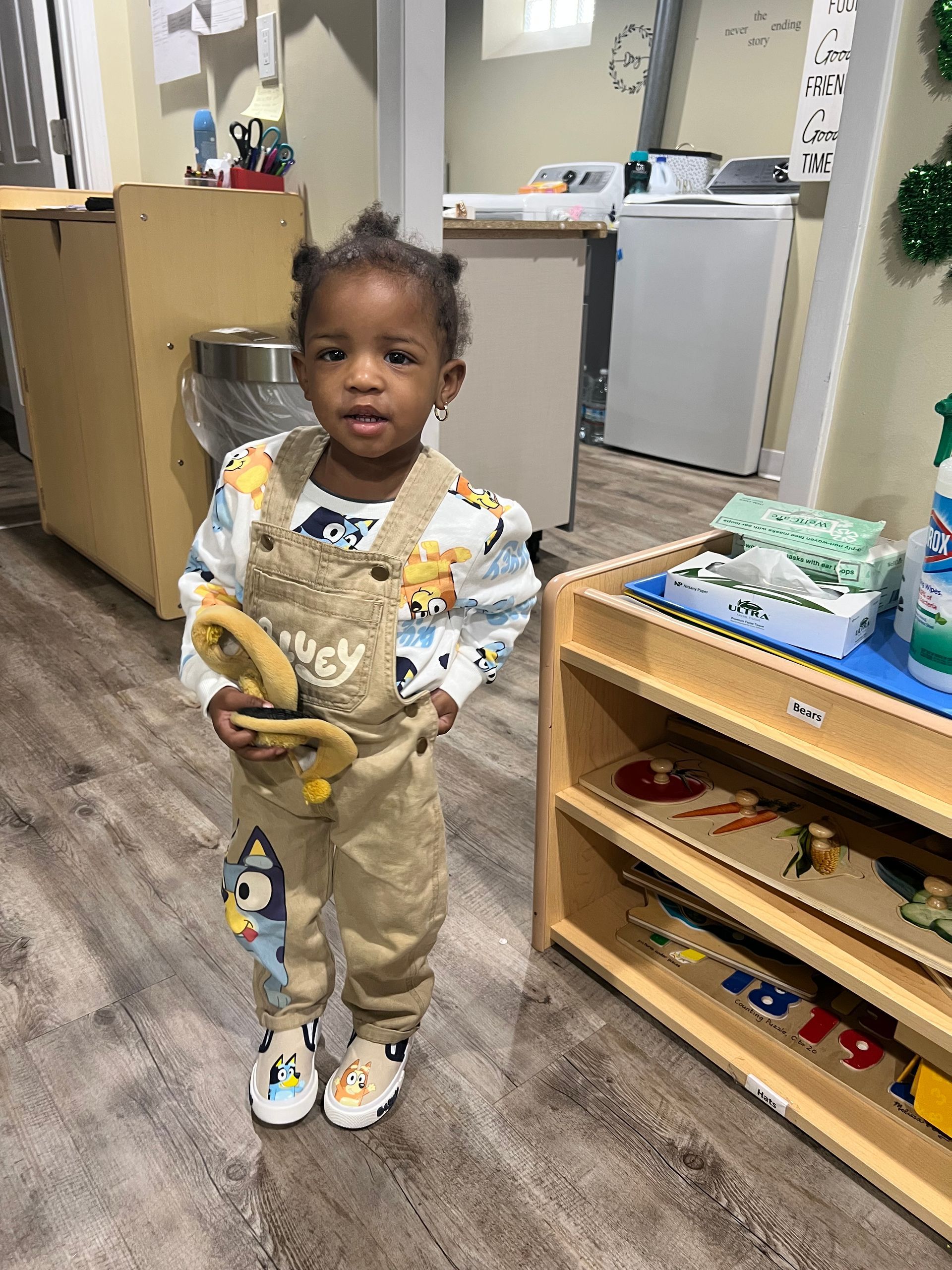 A little girl is standing in a room holding a banana.