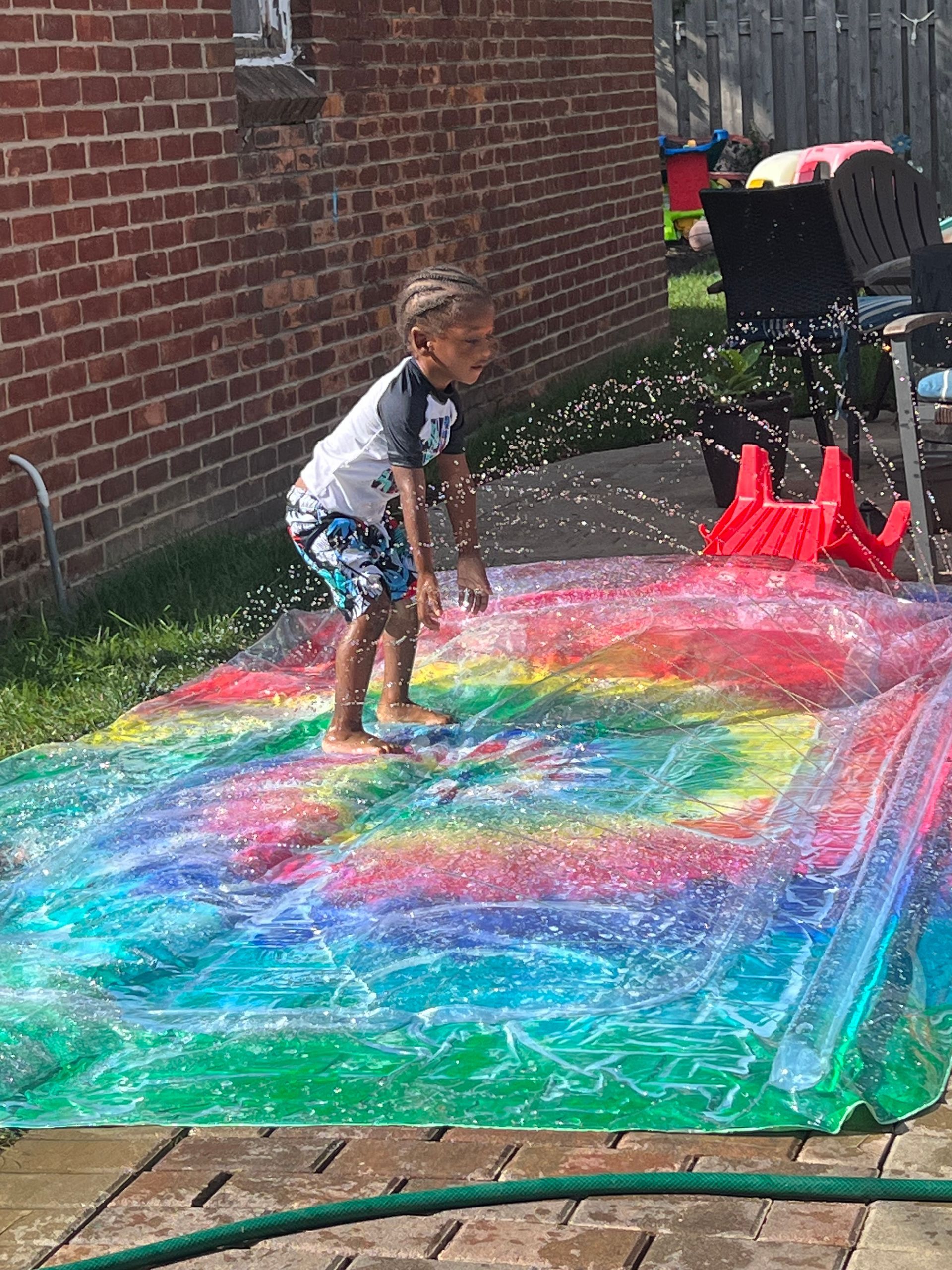 A young boy is playing on a rainbow water slide.