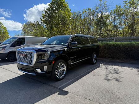 Black GMC Yukon SUV, front view. Dark gray grille, red GMC badge, black wheels.