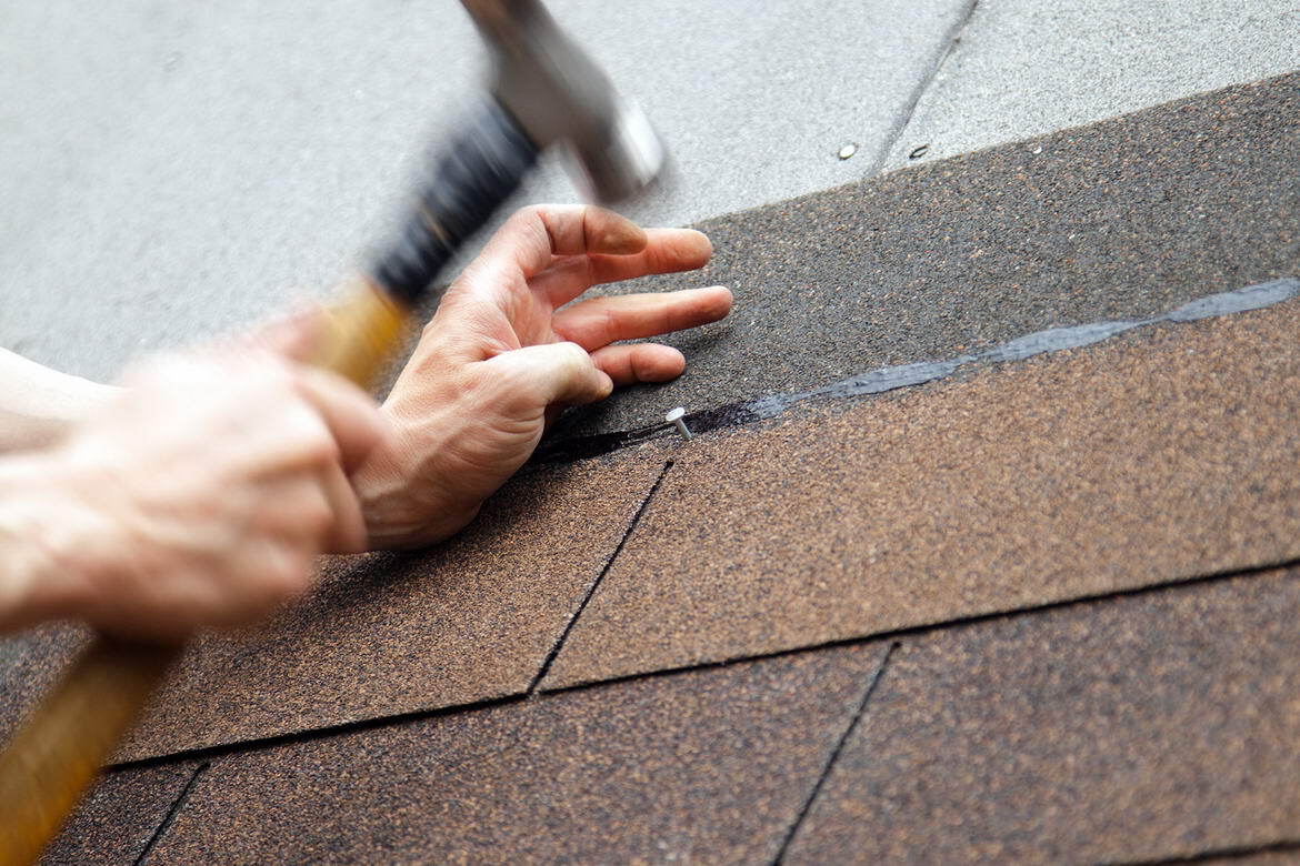 A person is using a hammer to fix a roof shingle.