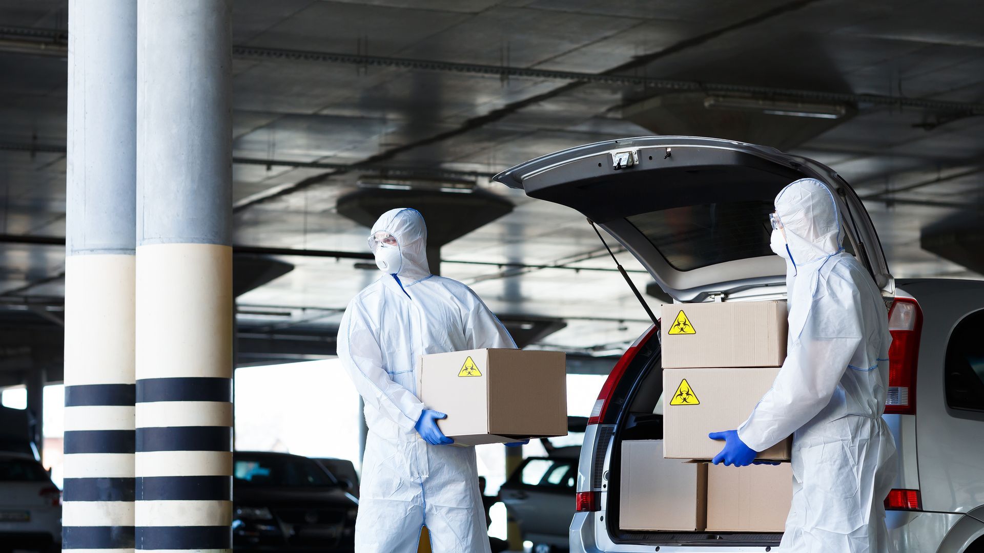Dos hombres con trajes de protección están cargando cajas en la parte trasera de un automóvil.