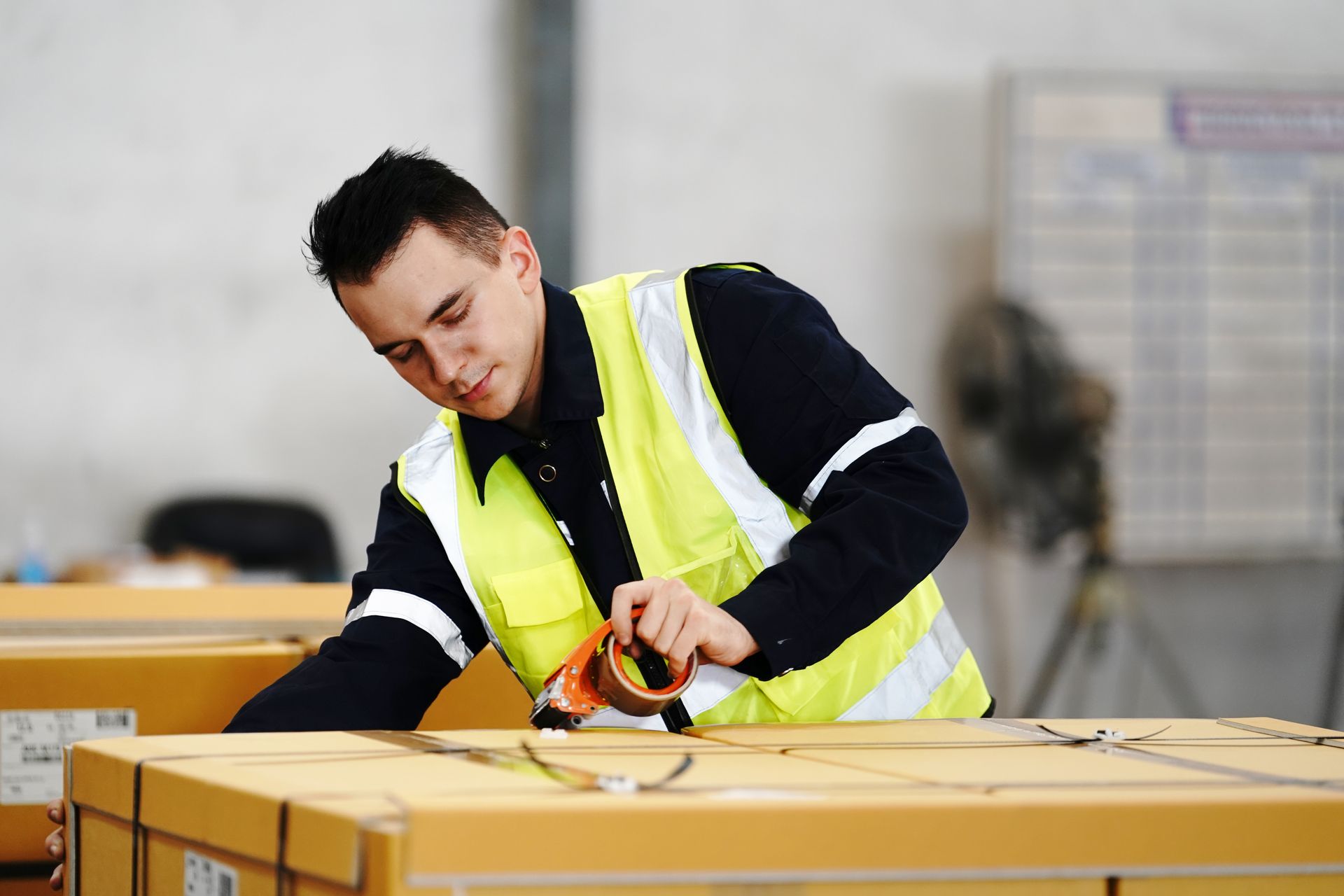 Un hombre con un chaleco amarillo está envolviendo una caja con cinta adhesiva.