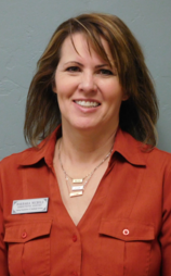 Woman with light brown hair, smiling, wearing a rust-colored shirt and necklace.