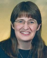 Woman with glasses, brown hair, smiling at the camera.