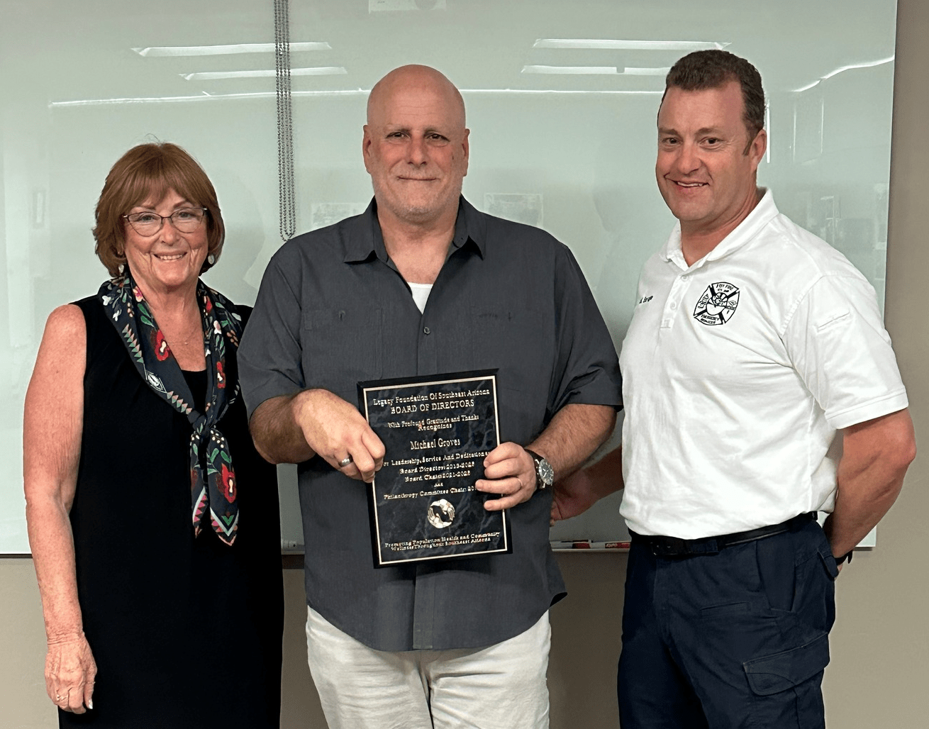 Three people smiling, posing with an award plaque indoors.
