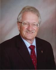 Man in suit, glasses, and red tie smiles. Portrait on a gradient background.