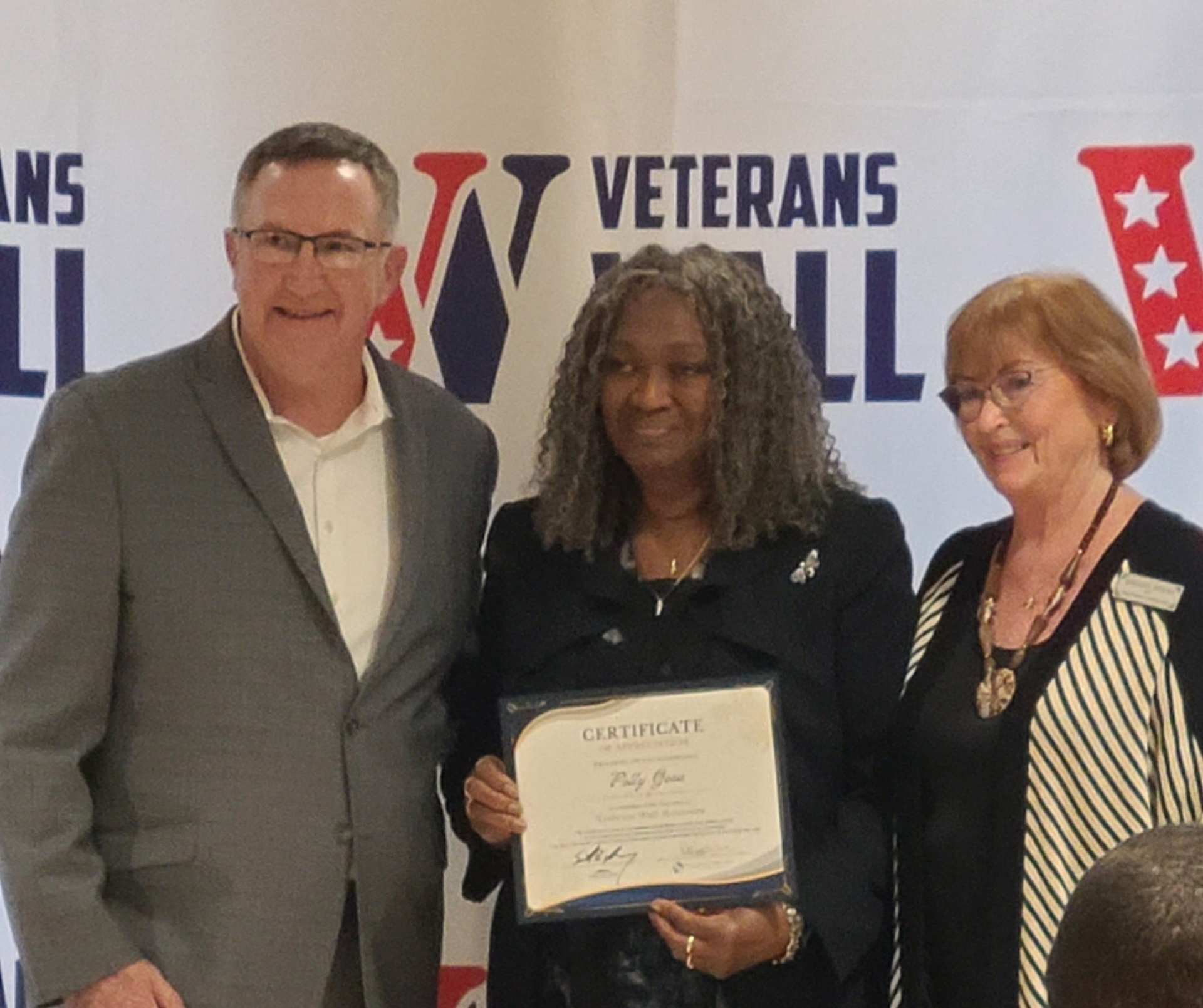 Group of people smiling, posing for a photo in a room with a banner; several hold papers.