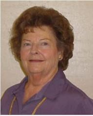 Woman with curly brown hair wearing a purple shirt, smiling, gold necklace.