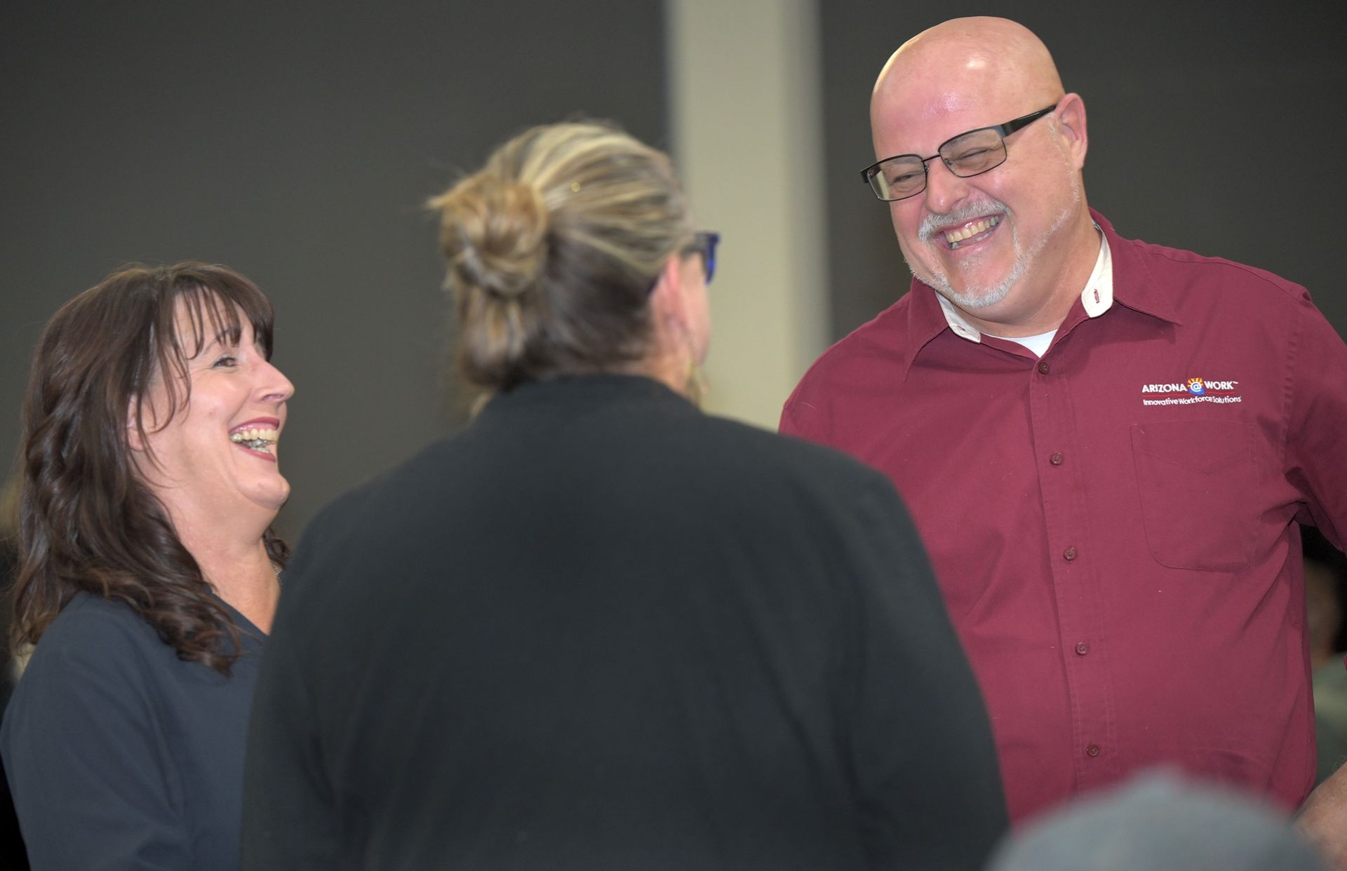 Large conference room with people seated at tables. Two screens display presentations.
