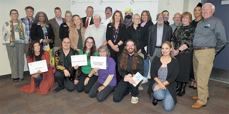 Large conference room with people seated at tables. Two screens display presentations.