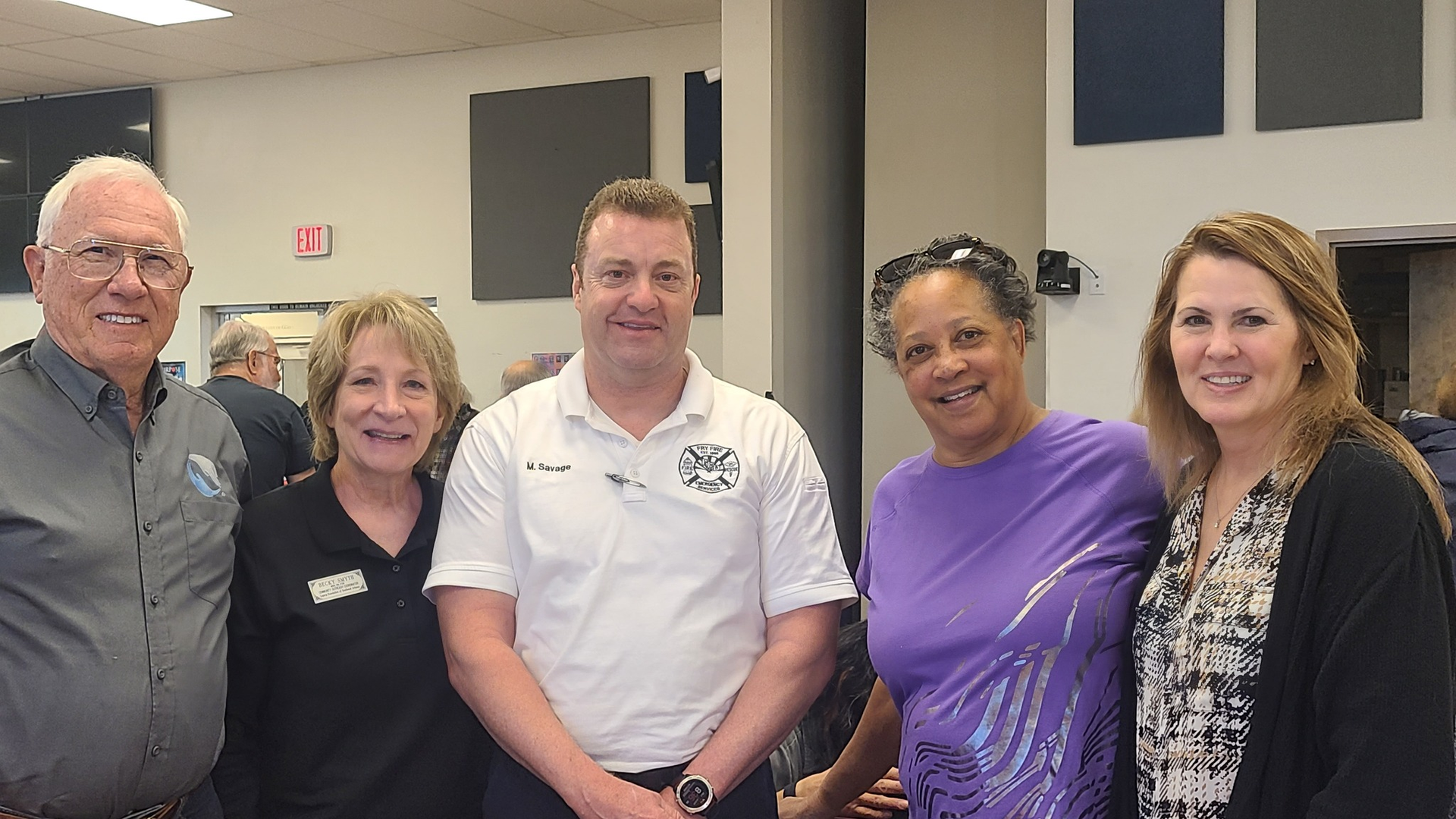Two men hold a plaque. Older man in red shirt presents it to a bald man in pink shirt. Office setting.