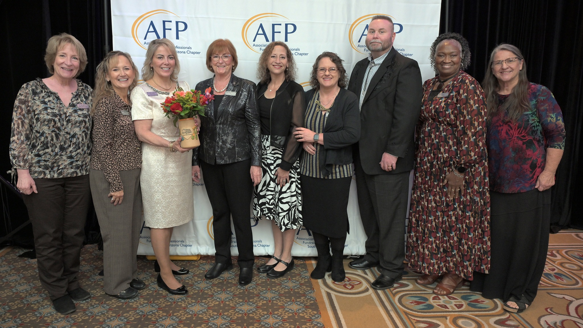 Large conference room with people seated at tables. Two screens display presentations.
