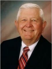 Smiling older man in a dark suit, white shirt, and red-striped tie.