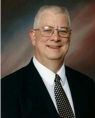 Man with glasses wearing a black suit smiles at the camera.