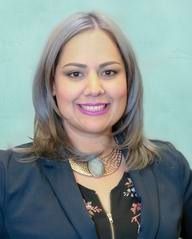 Woman with silver hair, smiling, wearing a blazer and necklace.