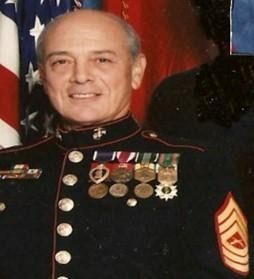 Man in Marine dress uniform, smiling, with medals, in front of an American flag.