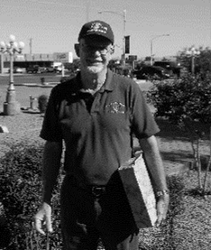 Man in cap and polo shirt holding brick outside on sunny day.