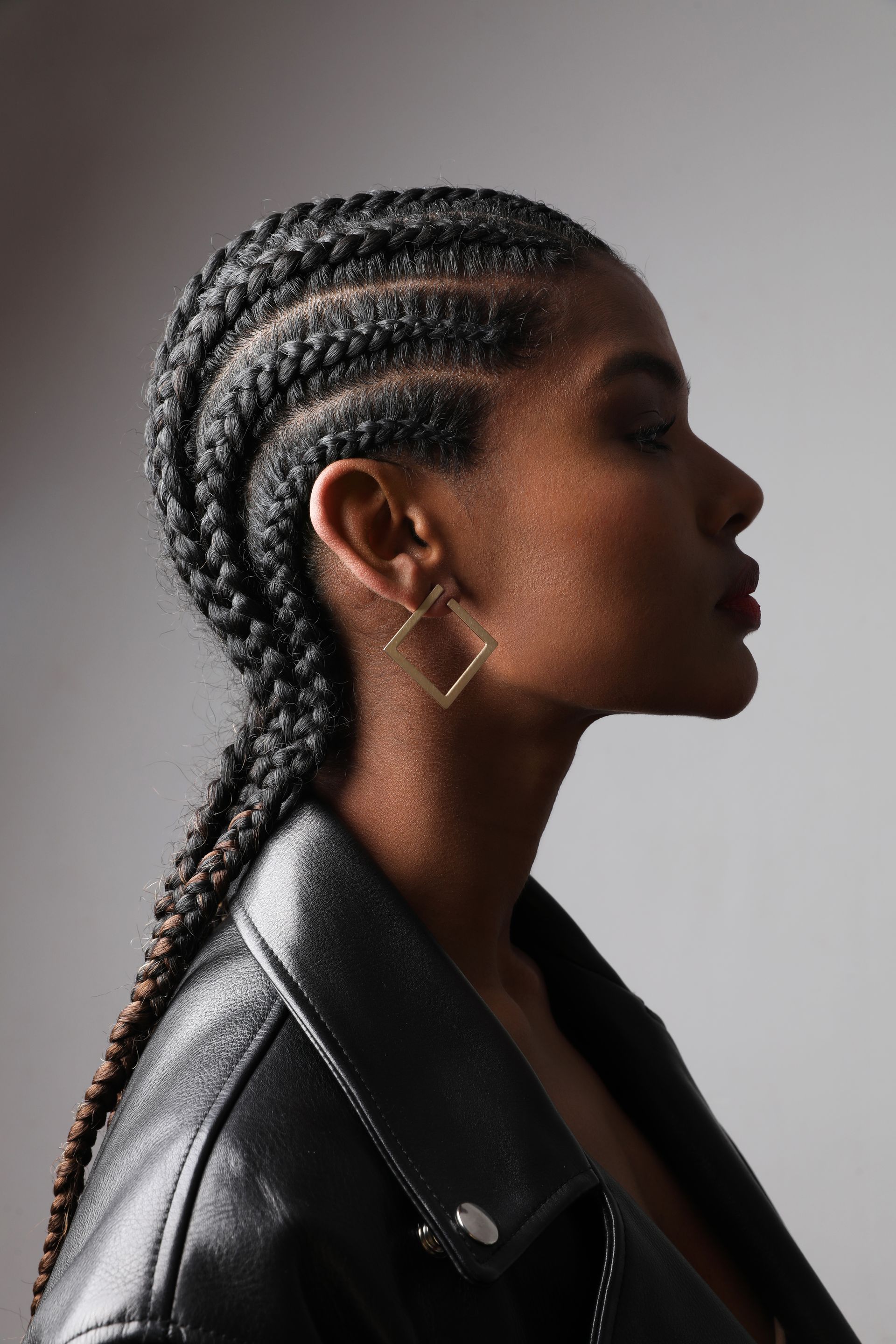 Side profile of a person with braided hair wearing a black leather jacket against a gray background