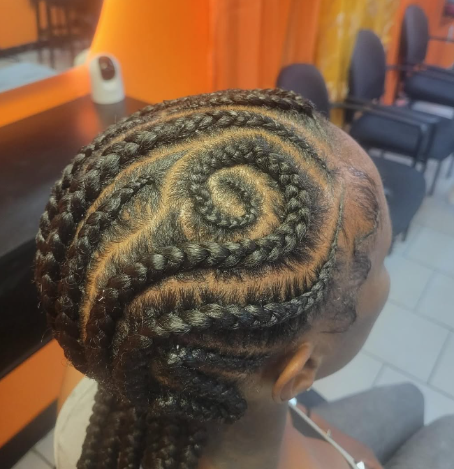 Braided updo with a floral bun, seen from the back in a salon setting, with “Hair By Adama” text overlaid