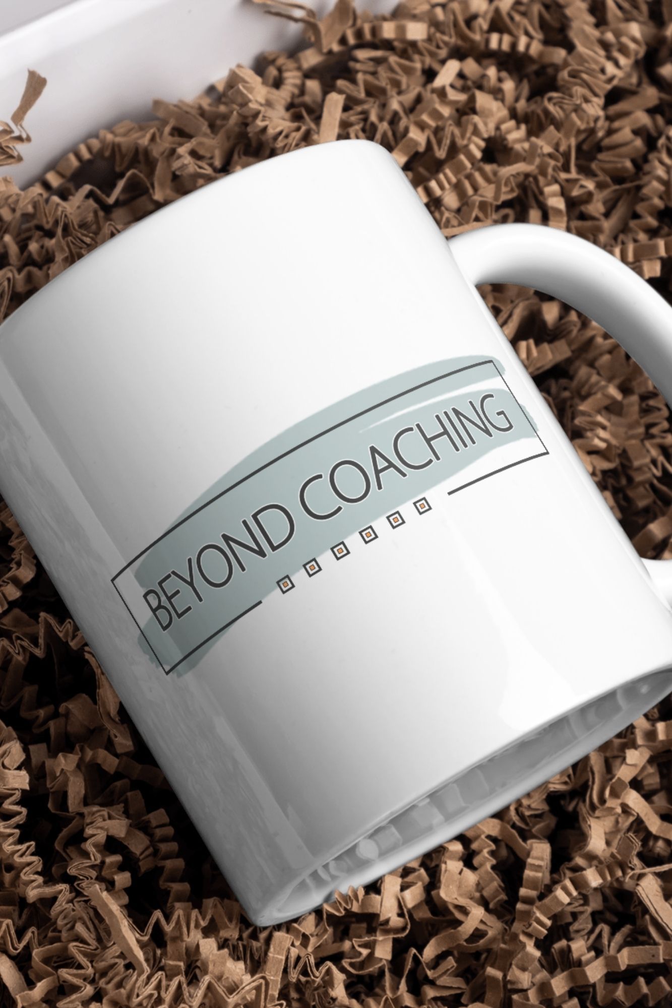 A white coffee mug with the words beyond coaching on it is sitting on a pile of shredded paper.