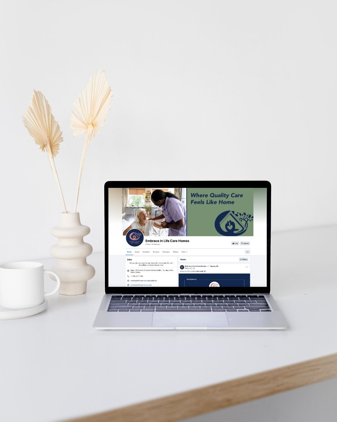 A laptop computer is sitting on a desk next to a vase of dried flowers.