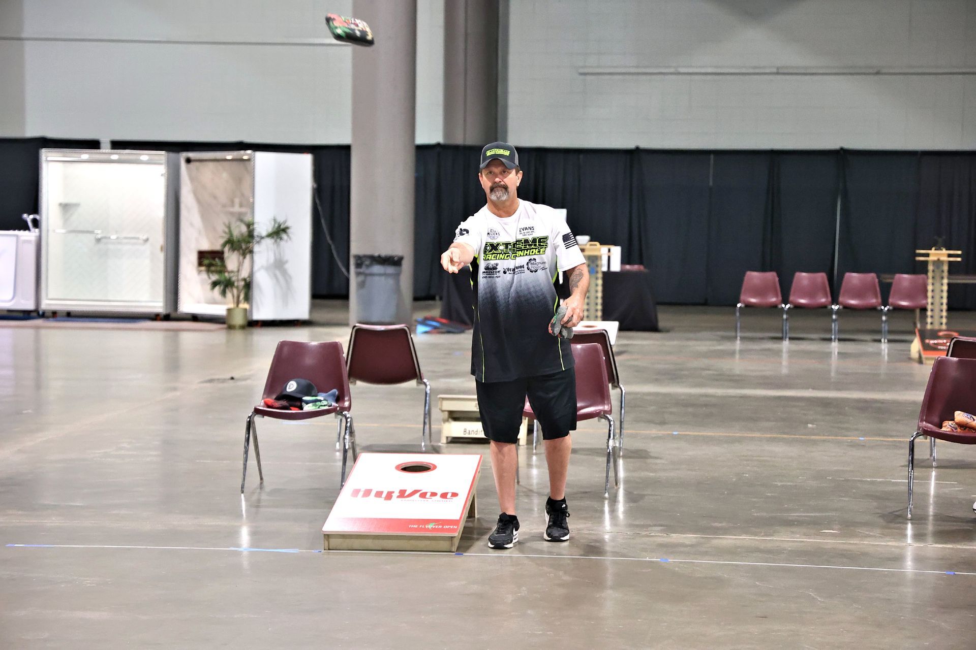A man is throwing a frisbee at a cornhole board in an empty room.