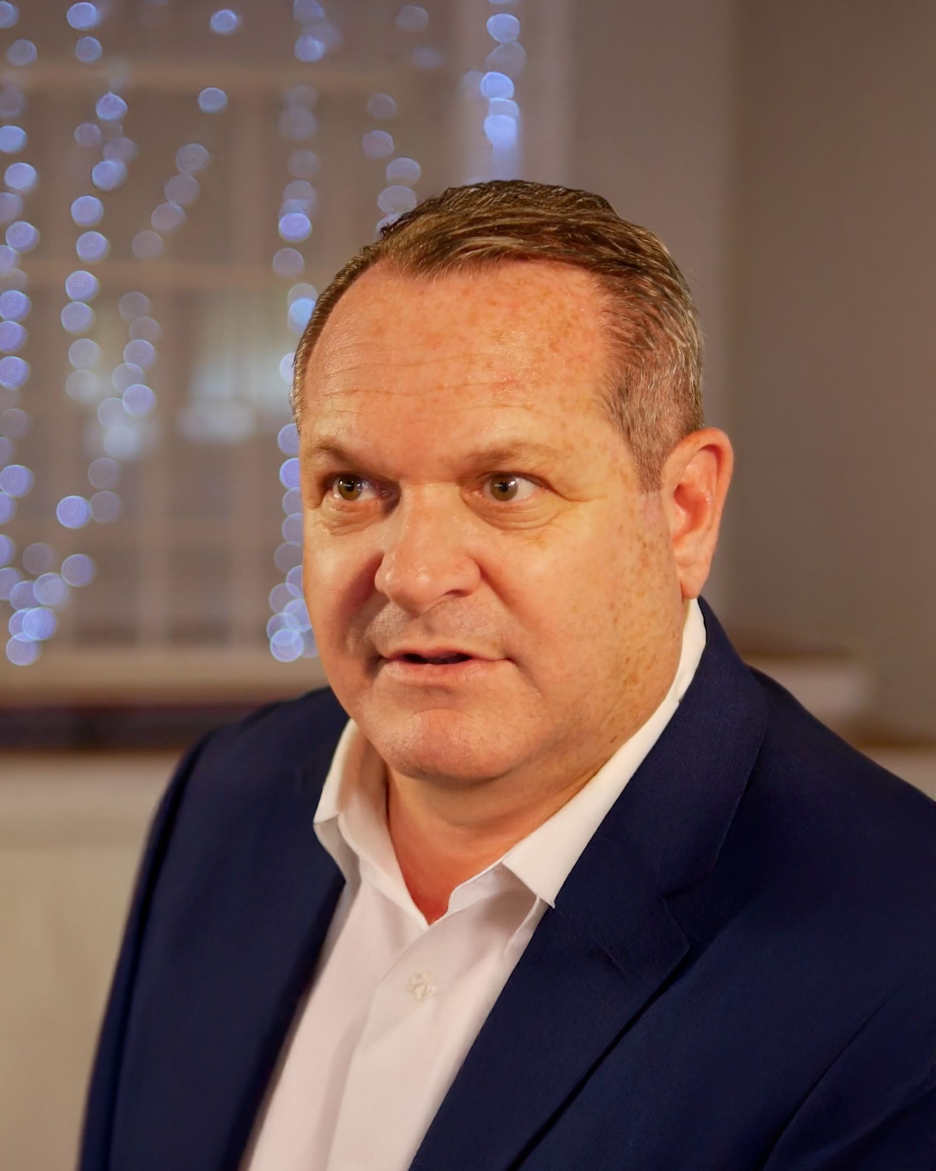 A man in a blue suit and white shirt is looking at the camera