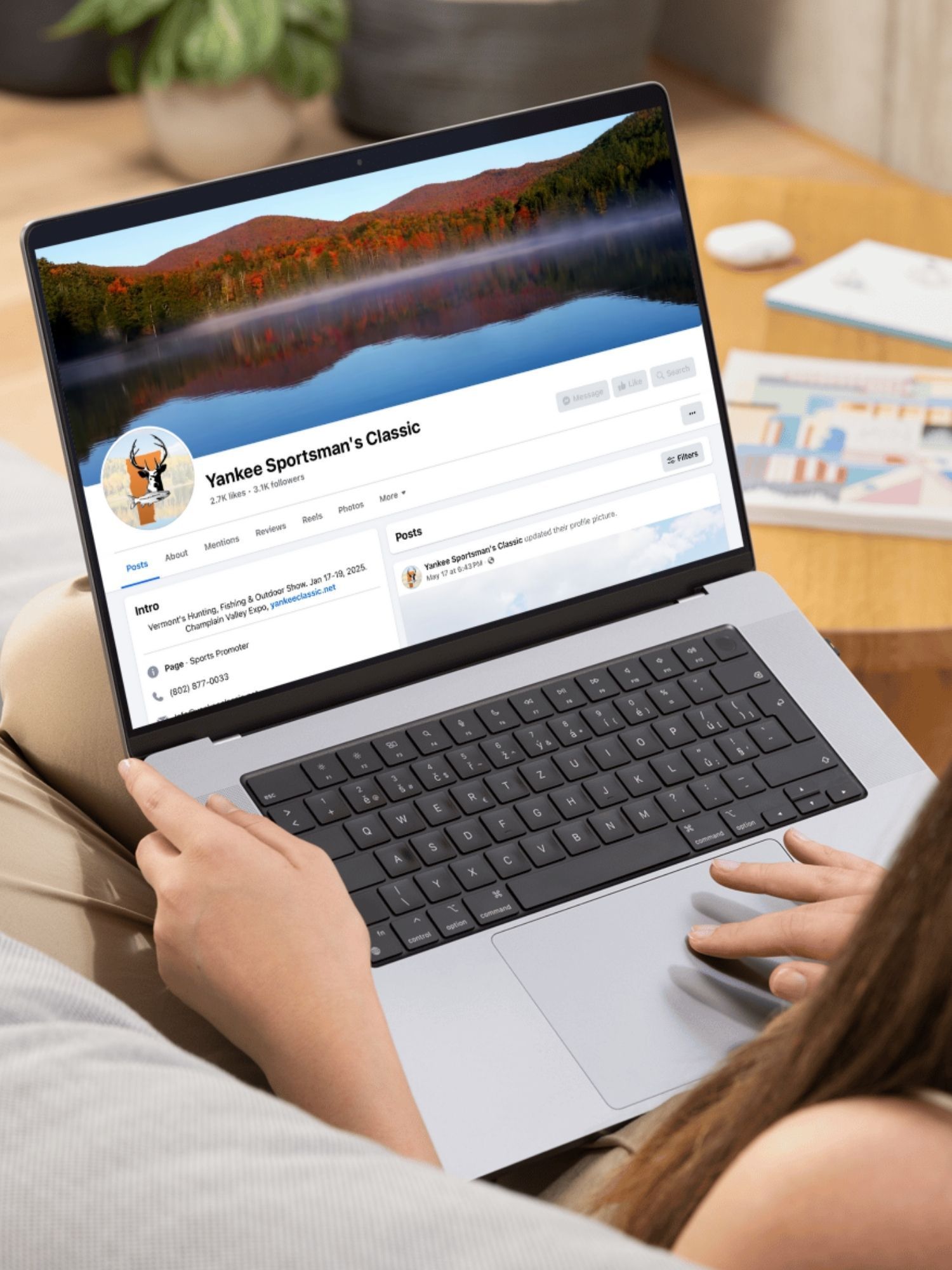 A laptop computer is sitting on a desk next to a vase of dried flowers.