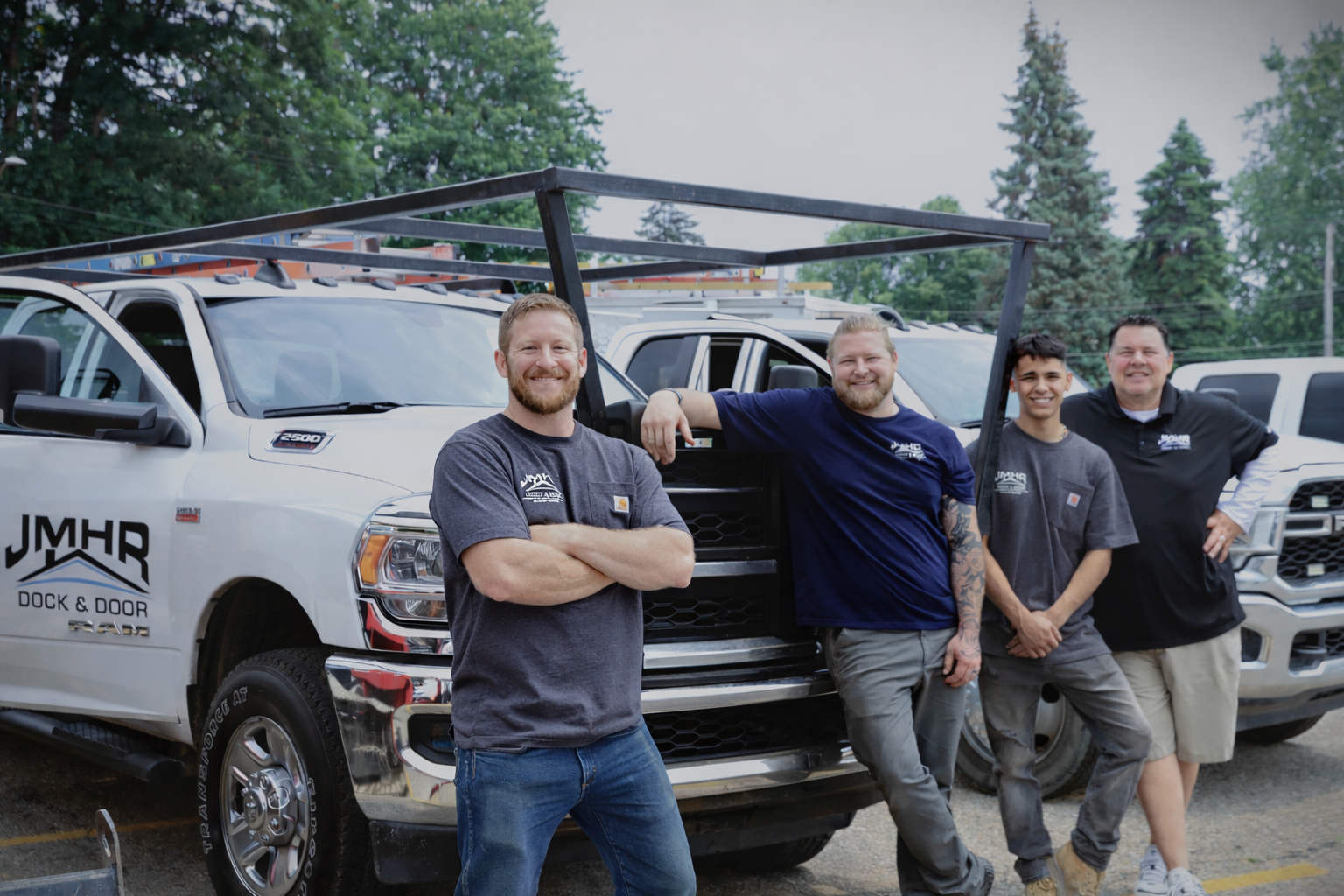 Four men pose with work trucks; one leans on the hood. Logo on truck reads JMHR Deck & Fence.
