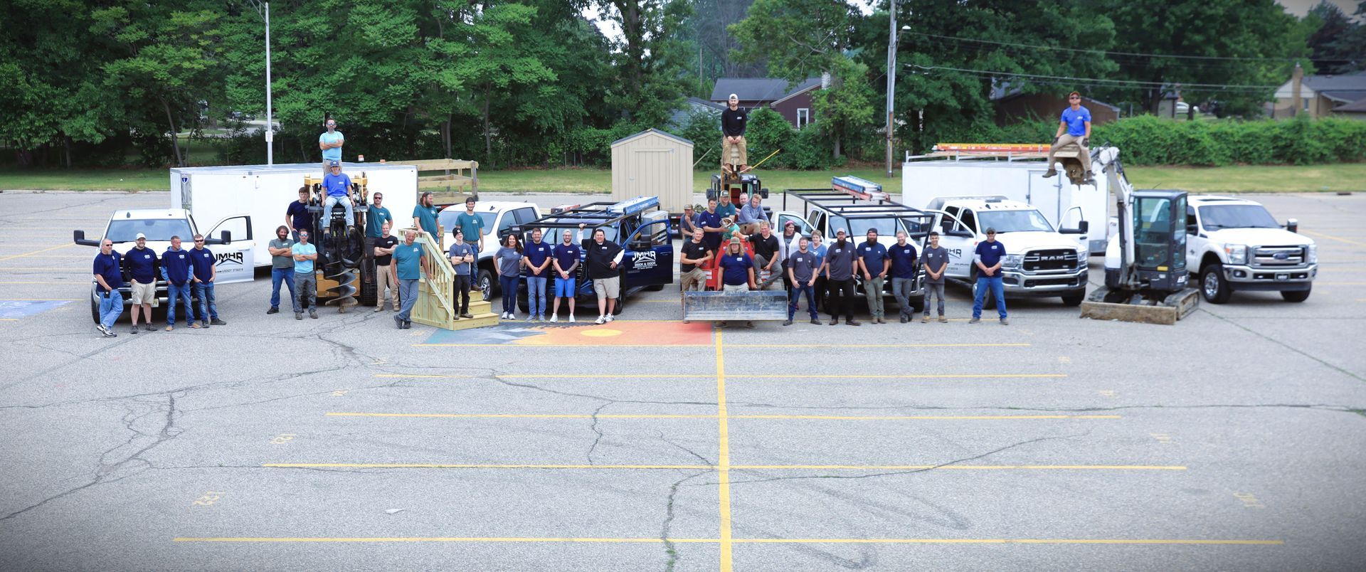 Group of people standing with trucks in a parking lot. Some are on top of the vehicles, trees in the background.